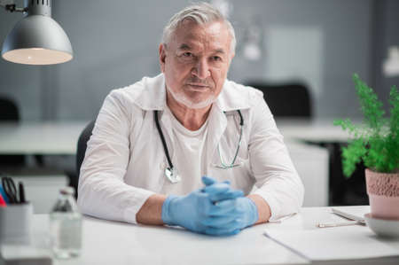 The impressive head doctor of the clinic sits in his office and poses for the cameraの写真素材