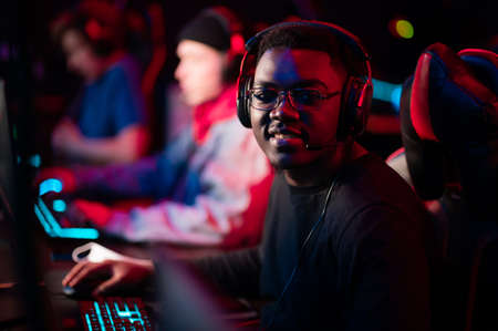 Neon light in the arena at the online shooter tournament. A young black cyber athlete looks at the camera. Blurred background.の写真素材