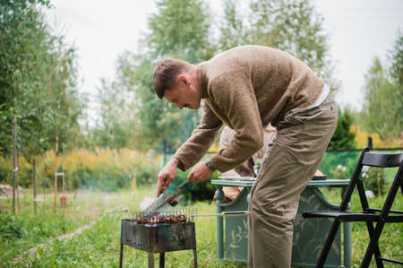A young eastern european man prepares a barbecue, roasts fragrant meat on the grill. Concept of a romantic picnic for a young couple.の写真素材