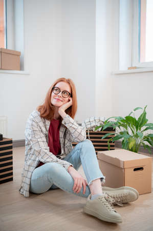 A pretty young woman with glasses is tired when moving to a new apartment, she sits on the floor...