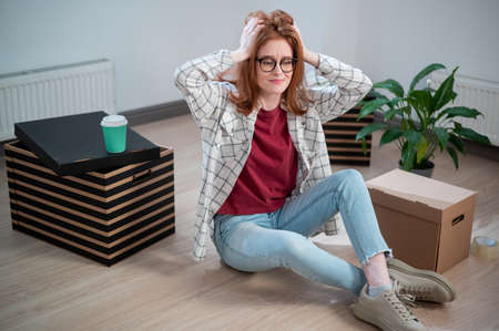 During the move to a rented apartment, a young woman with glasses sat on the floor from fatigue and...