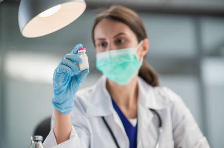 A young female lab technician wearing a medical mask shows off a coronavirus vaccine in her lab at the hospitalの写真素材