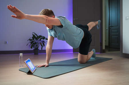 Online training of a young athlete at home on the mat, a professional coach conducts a class on the Internetの写真素材