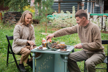 A young couple celebrates their wedding anniversary on a country plot. They roast meat, drink beer, relax in nature.の写真素材