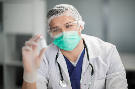 A young, handsome lab technician in safety glasses examines a new vaccineの写真素材