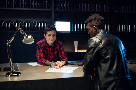 Black guy chooses a tattoo sketch in a tattoo studio. He is helped by a young pretty administrator tattoo artist girl.の写真素材