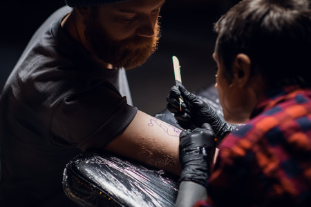 A tattoo artist with short hair and piercings is preparing to get a tattoo on a mans arm in a tattoo parlorの写真素材