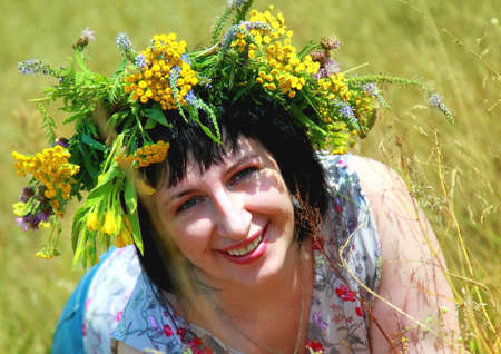 A young woman with a smile on her face and a wreath of wildflowers on her head, basking in the rays of the summer sun.の写真素材
