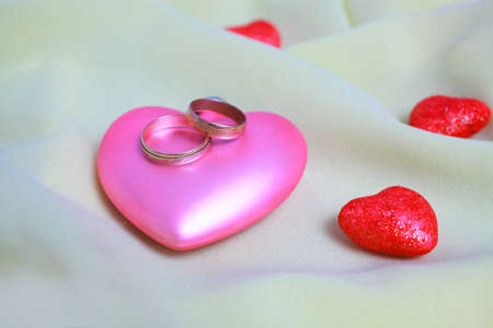 The light transparent silk like background. On the silk are decorative hearts with wedding rings close up.の写真素材