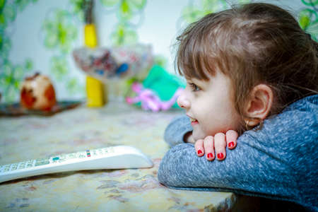 The baby sits at the table, next to the TV remoteの写真素材