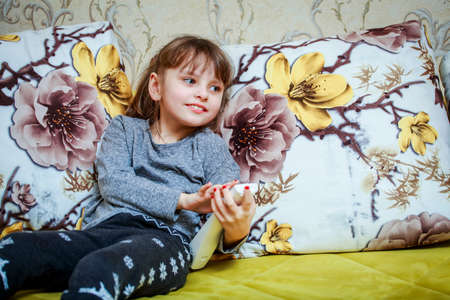 A little cheerful girl presses the button on the TV remote.の写真素材