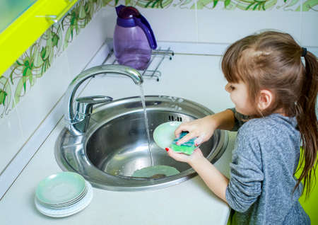 Little girl helps mother to wash the dishes in the kitchen.の写真素材