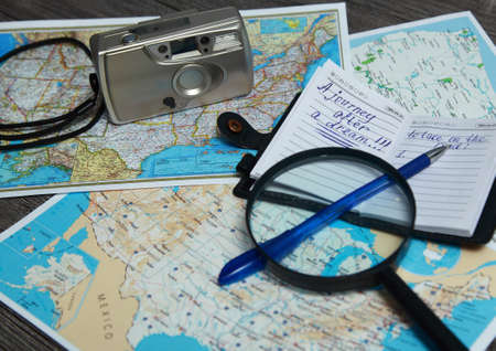 On the table is an Atlas of the United States. There is a notebook with notes and a pen, as well as a magnifying glass and a camera.の写真素材