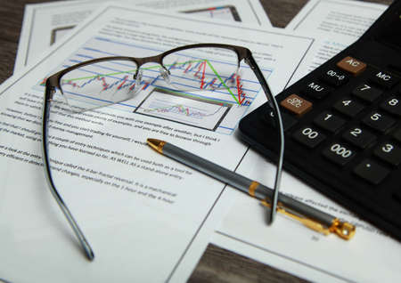 On the table are financial documents with a chart, calculator, glasses and pen.の写真素材