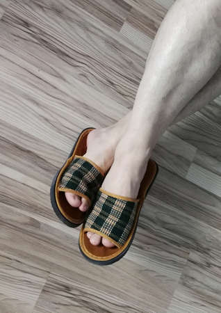 Mens foots in slippers on the background of the parquet floorの写真素材
