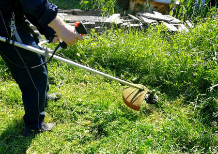 Mens hands holding a lawn mower and cut the grass on the site.の写真素材