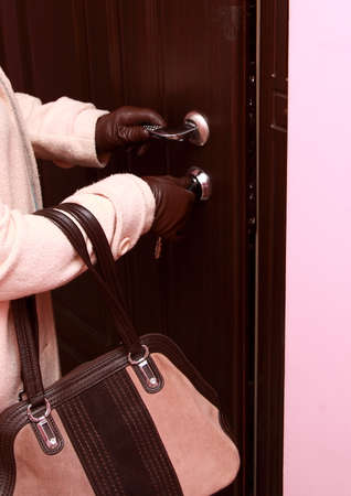 A woman in a coat, gloves and with a bag in her hands opens the front door.の写真素材