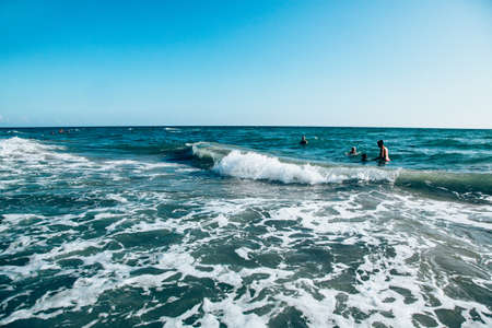 A storm at sea and waves with foam coming to the shore. Family swimming in the sea.のeditorial素材