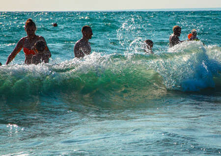 Storm at sea. A large wave closes bathing people. People enjoy the waves and splashes.