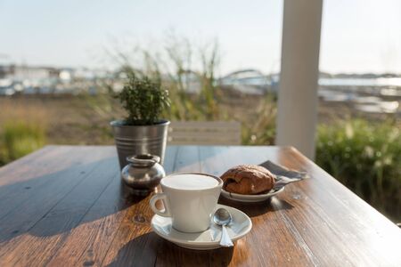 Breakfast of cappuccino and pastry at the beachの写真素材