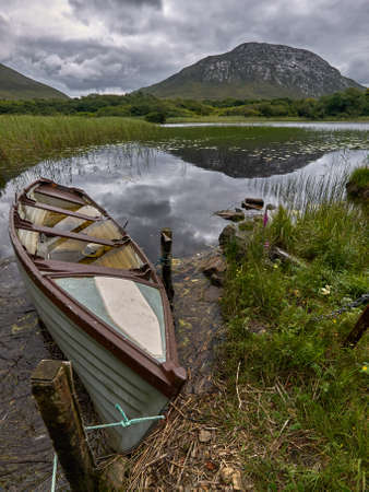 A boat tied to a rope at the shore of a beautiful lake surrounded by mountains