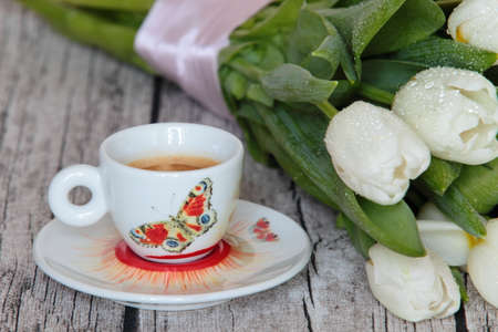 Beautiful white tulips and a cup of coffee on wooden backgroundの写真素材