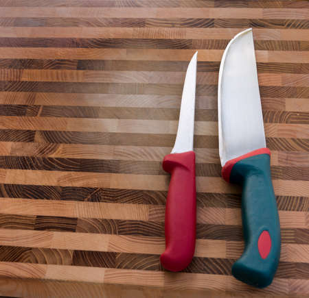 two meat knives with red and green handles on wooden cutting board, top viewの写真素材