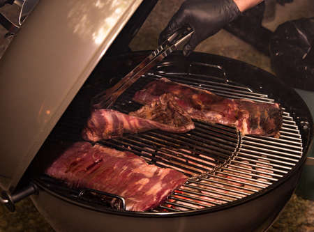 hand of man in black glove with tongs turns beef skirt steak on barbecue grillの写真素材