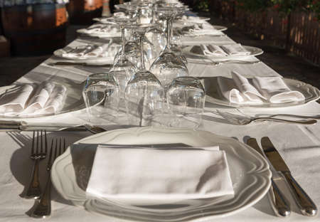 Dining table set with crockery, forks, knives, wine glass, glass of water and white napkin in the restaurant, outsideの写真素材