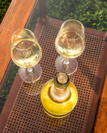 two glasses of wine and a bottle of white wine on a glass top with vienna straw in the background....