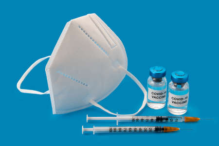 FFP2 - KN95 mask and Coronavirus COVID-19 vaccine. Vials with syringes with mask isolated on blue...