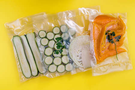 vacuum vegetables, sliced cauliflower zucchini and yellow peppers in vacuum packed sealed for sous vide cooking on yellow backgroundの写真素材