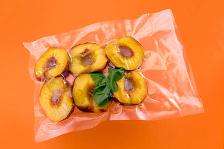 Peaches cut in half with mint leaves in vacuum packed sealed for sous vide cooking on orange backgroundの写真素材