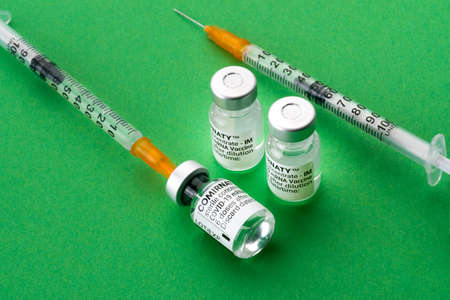 TURIN, ITALY - JULY 27, 2021: Pfizer-BioNTech COVID-19 Vaccine Comirnaty vials, two Original vaccine vials with syringes on green backgroundのeditorial素材
