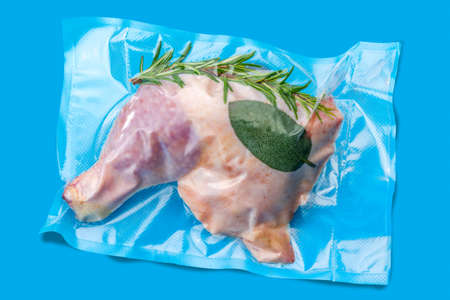 Whole chicken thighs with rosemary and sage in vacuum packed sealed for sous vide cooking isolated on blue backgroundの写真素材