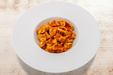 Typical agnolotti del plin, stuffed egg pasta ravioli from Langhe, Piedmont, Italy, seasoned with tomato sauce in white dish on wooden tableの写真素材