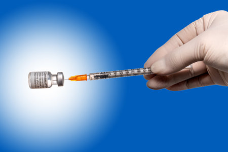 Turin, Italy - December 18, 2021: Pfizer-BioNTech COVID-19 Vaccine Comirnaty vials, hand with latex glove with syringe drawing vaccine dose from vial original vaccine vials, on blu backgroundのeditorial素材