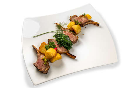 Roasted lamb chops with potatoes, spinach and herbs on white plate isolated on whiteの写真素材