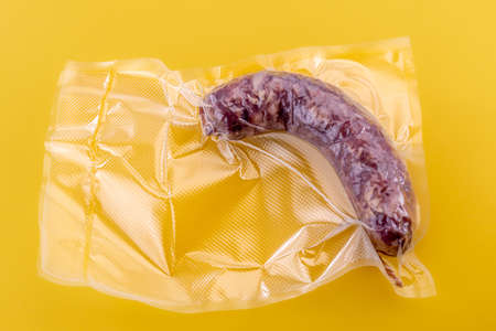 Italian salame sausage in vacuum packed sealed for sous vide cooking isolated on yellow background...