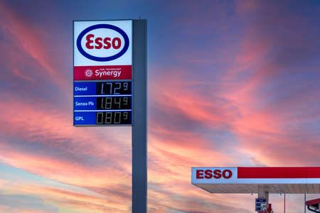 Fossano, Italy - February 22, 2022: Esso logo sign with fuel Euro price display on colorated sunset sky, Esso is a brand of the global oil industry giant ExxonMobil. Expensive fuel price concept.のeditorial素材