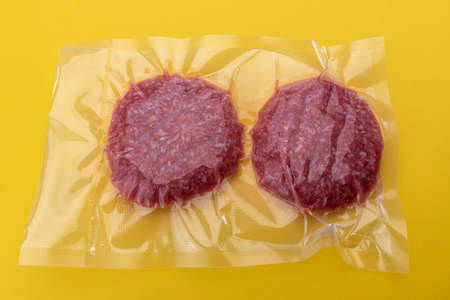 Burger meat for hamburger in vacuum packed sealed for sous vide cooking isolated on yellow...
