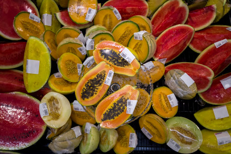 Cantaloupe melon, watermelon and papaya, cut in half packed in plastic film displayed and priced in euro for sale in supermarket fridge, top view, ready to eatの写真素材