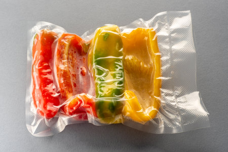 Slices of yellow red and green peppers in vacuum-sealed package for sous vide cooking ion gray backgroundの写真素材