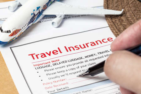 Travel Insurance Claim application form and hat with eyeglass and human hand holding pen, business insurance and risk concept; document and plane is mock-upの写真素材