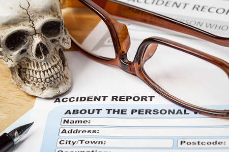 Accident report application form and human skull on brown envelope and eyeglass, business insurance and risk concept; document is mock-upの写真素材
