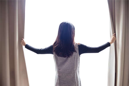 Asian portrait beautiful woman opening curtainsの写真素材