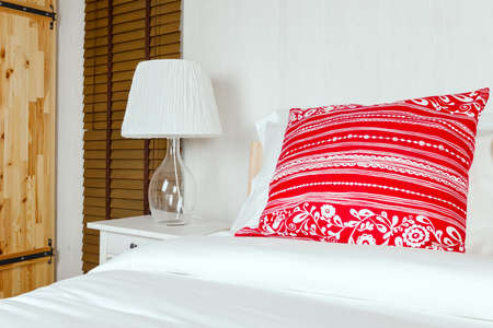 Red pillow on bedroom with white bed sheet and lampの写真素材