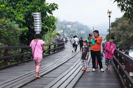 SANGKHLABURI, THAILAND - DECEMBER 27, 2015: tourist taking photo person turn goods on head, walking on Sapan Mon, wooden bridge in morning in Sangkhlaburi, Kanchanaburi Thailand,on December 27, 2015のeditorial素材