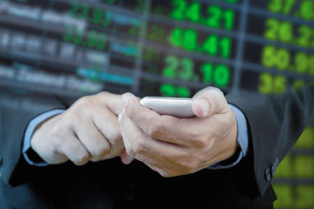 Businessman touch smart phone in hand with exchange rate blur backgroundの写真素材