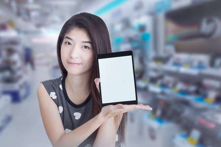 Young Asian woman show or display tablet with blank screen on shopping mall backgroundの写真素材